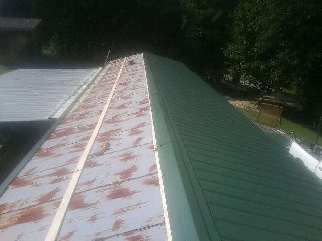 Old rusted panels beside newly installed green metal roofing — Wind Damage Roof Repair by Roofing Brothers in Youngsville