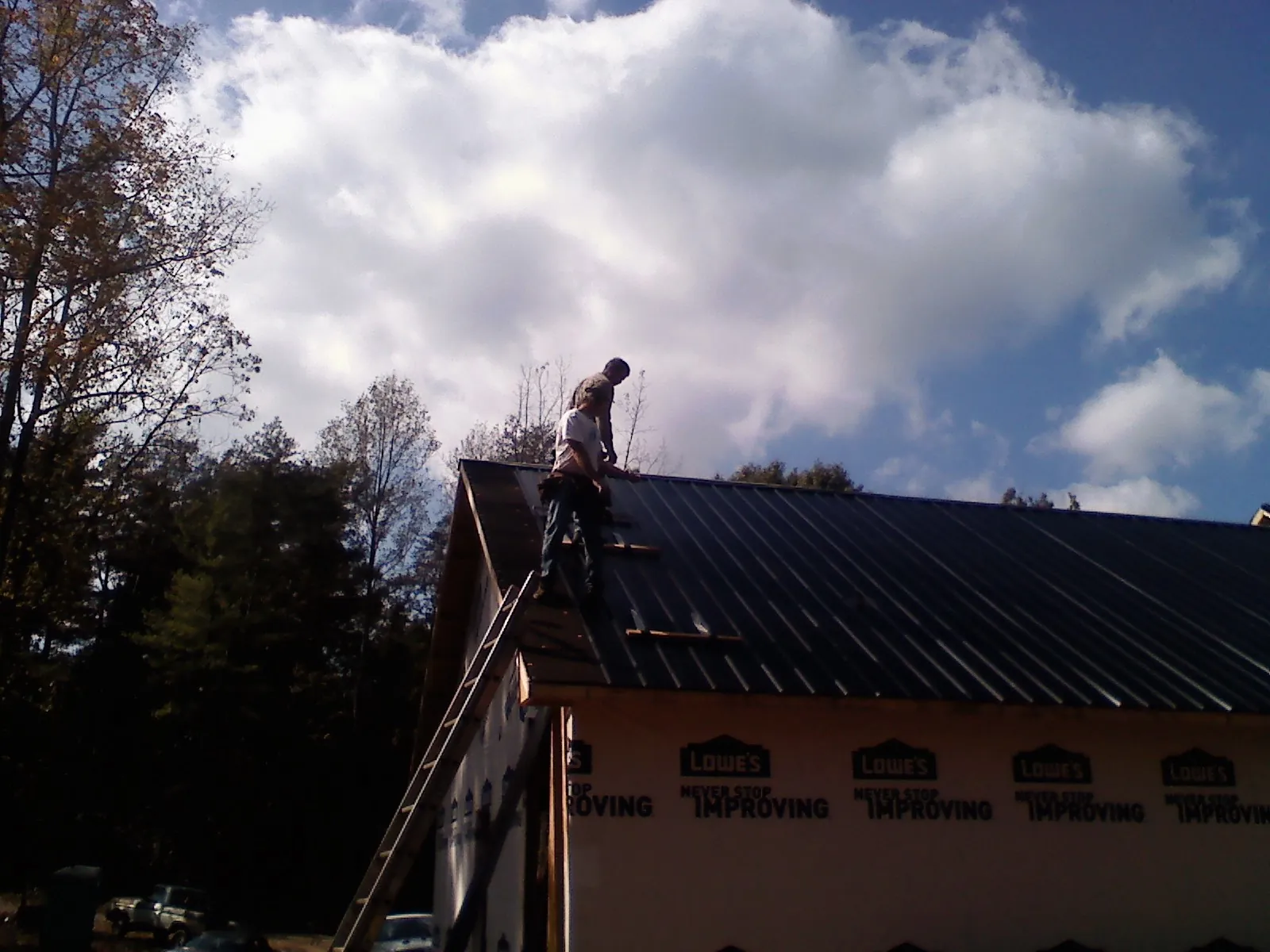 Roofer fastening dark metal panels high against a cloudy sky, from a Roof Inspection job in Youngsville